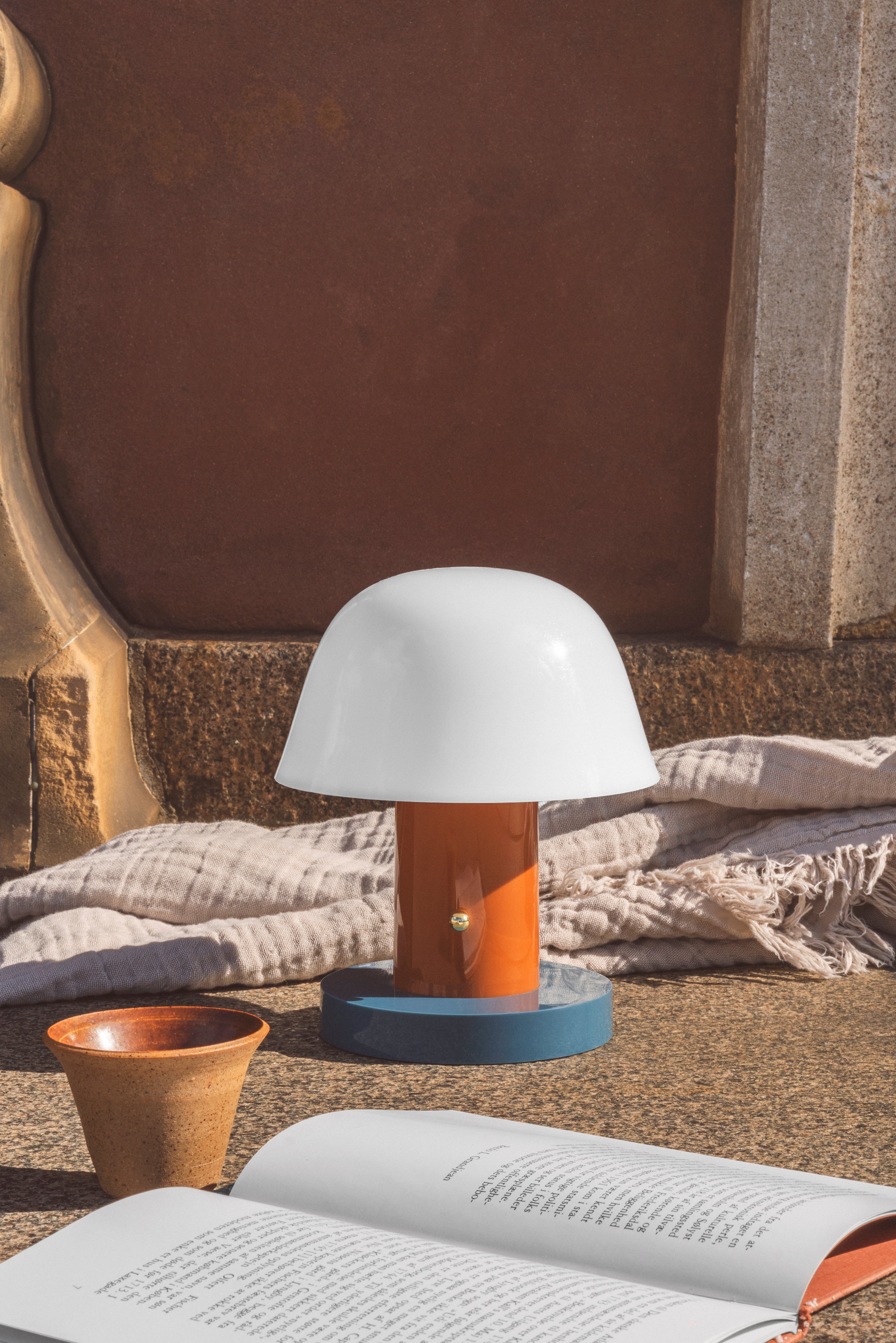Tragbare Lampe SETAGO JH27 mit cremefarbenem Schirm und orange-blauem Fuß.
